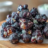 Freshly popped Black Currant Cheesecake Kettle Corn spills from a rustic pot, showcasing glossy kernels with a vibrant purple hue.