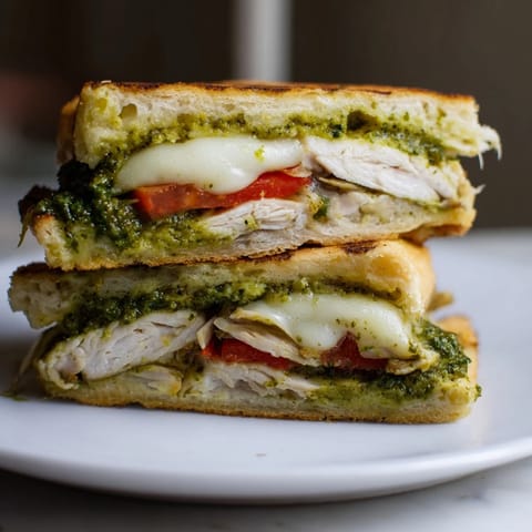 A toasted Chicken Pesto Panini cut in half, showing layers of sliced chicken, bright basil pesto, and arugula.