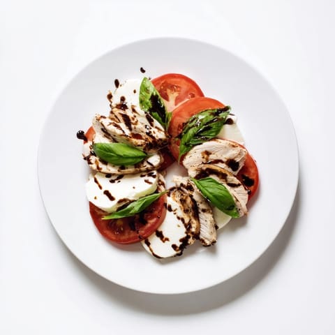 A vibrant Chicken Caprese Salad with juicy tomatoes, mozzarella, grilled chicken, and a drizzle of balsamic glaze.
