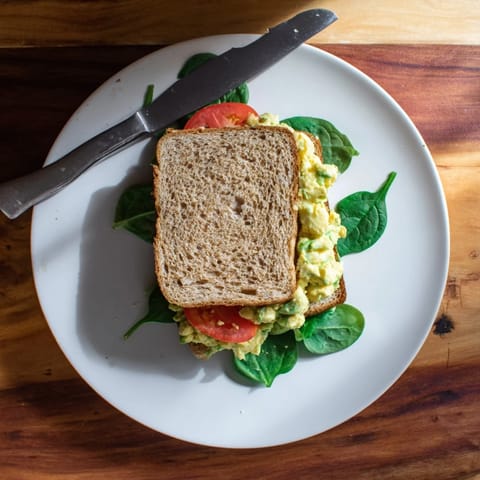 A close-up of a creamy avocado egg salad sandwich, showing the chunky texture and vibrant green and yellow hues.  