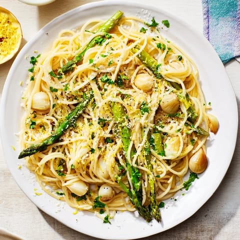 A close-up of steaming Roasted Garlic & Asparagus Pasta showing tender asparagus spears and melted Parmesan on spaghetti, ready to serve for a spring dinner.