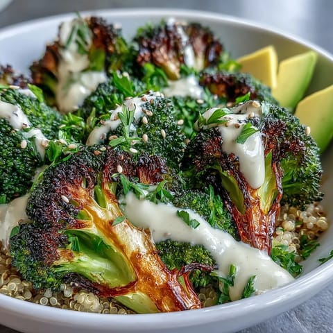 Golden roasted broccoli florets with crispy edges and charred red onion slices on a bed of fluffy quinoa, drizzled with creamy tahini sauce.  