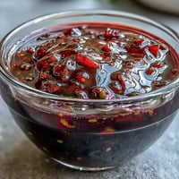 Vibrant black currant vinaigrette dressing in a glass jar with fresh herbs and berries on a rustic table.